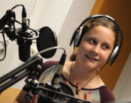 Mädchen im Hörfunkstudio vor Mikrofon, lächelnd