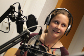 Mädchen im Hörfunkstudio vor Mikrofon, lächelnd