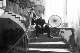CG2021_Albinobrothers_c_Albinobrothers Zu sehen sind die Bandmitglieder der Albinorothers auf Stufen in einem Treppenhaus sitzend, neben ihnen eine Bass Drum