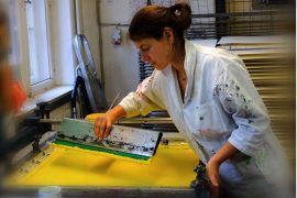 CG2021_GraceHelly_c_GraceHelly Auf dem Bild ist die Künstlerin Grace Helly in Arbeitskleidung zu sehen. Sie arbeitet mit Rakel an einem großen Sieb für Siebdruck