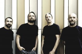UM4 2021 Das Foto zeigt die Mitglieder der Band UM4 - 4 Männer, im schwarzen T-Shirt entspannt vor einer Wand lehnend
