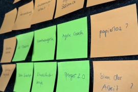 Wand mit Klebezetteln, auf denen verschiedene Begriffe stehen, z.B. Agile Coach, Pfleger 2.0, papierlos