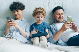 Bild: <a href="https://www.pexels.com/photo/a-family-with-a-little-son-sitting-on-a-bed-parents-looking-at-their-smartphones-and-their-son-playing-a-game-20459169/">Vitaly Gariev auf pexels</a>