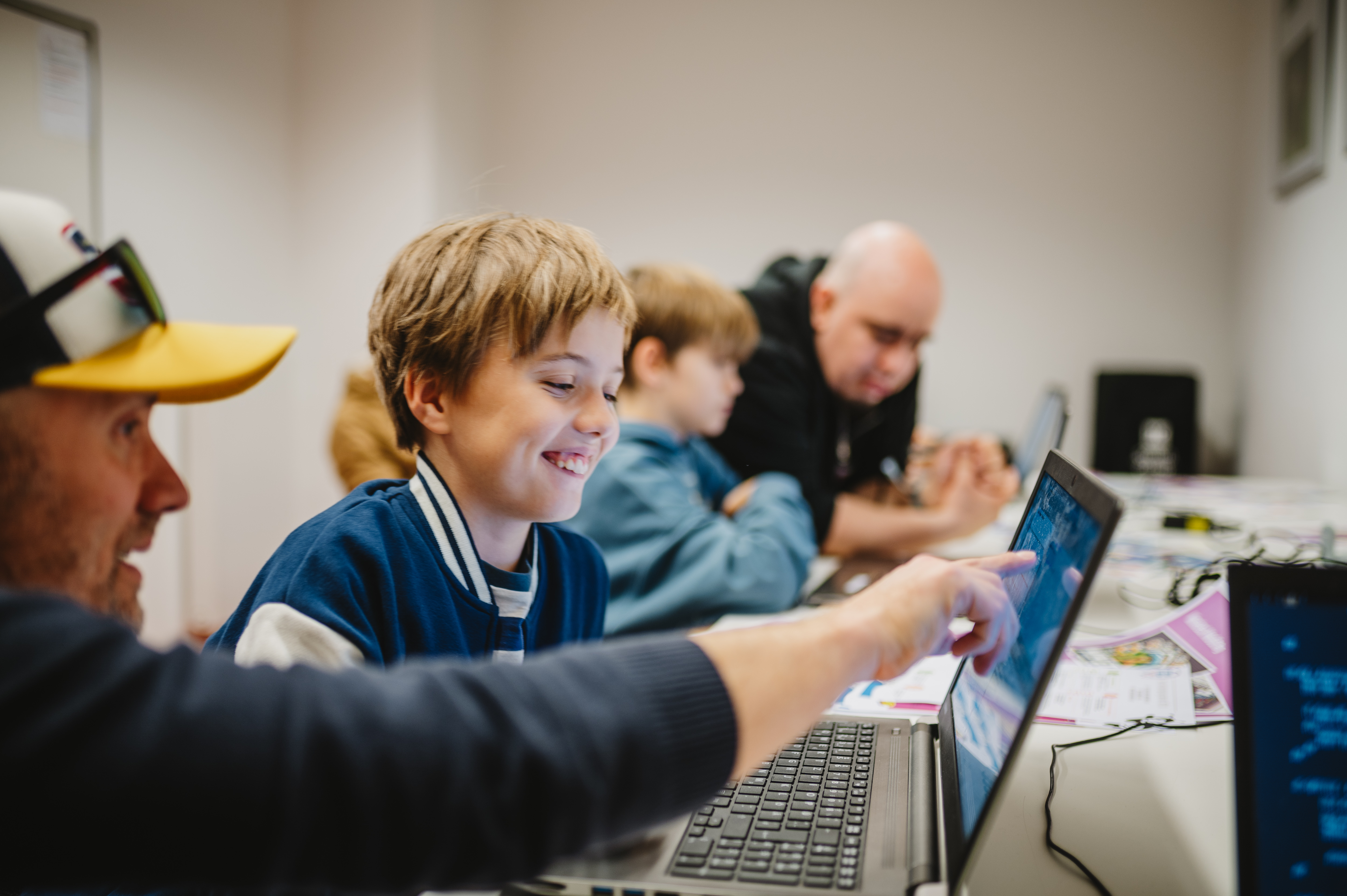 Mehrere Personen sitzen an einem Tisch und arbeiten an Laptops, eine Person zeigt auf einen Bildschirm