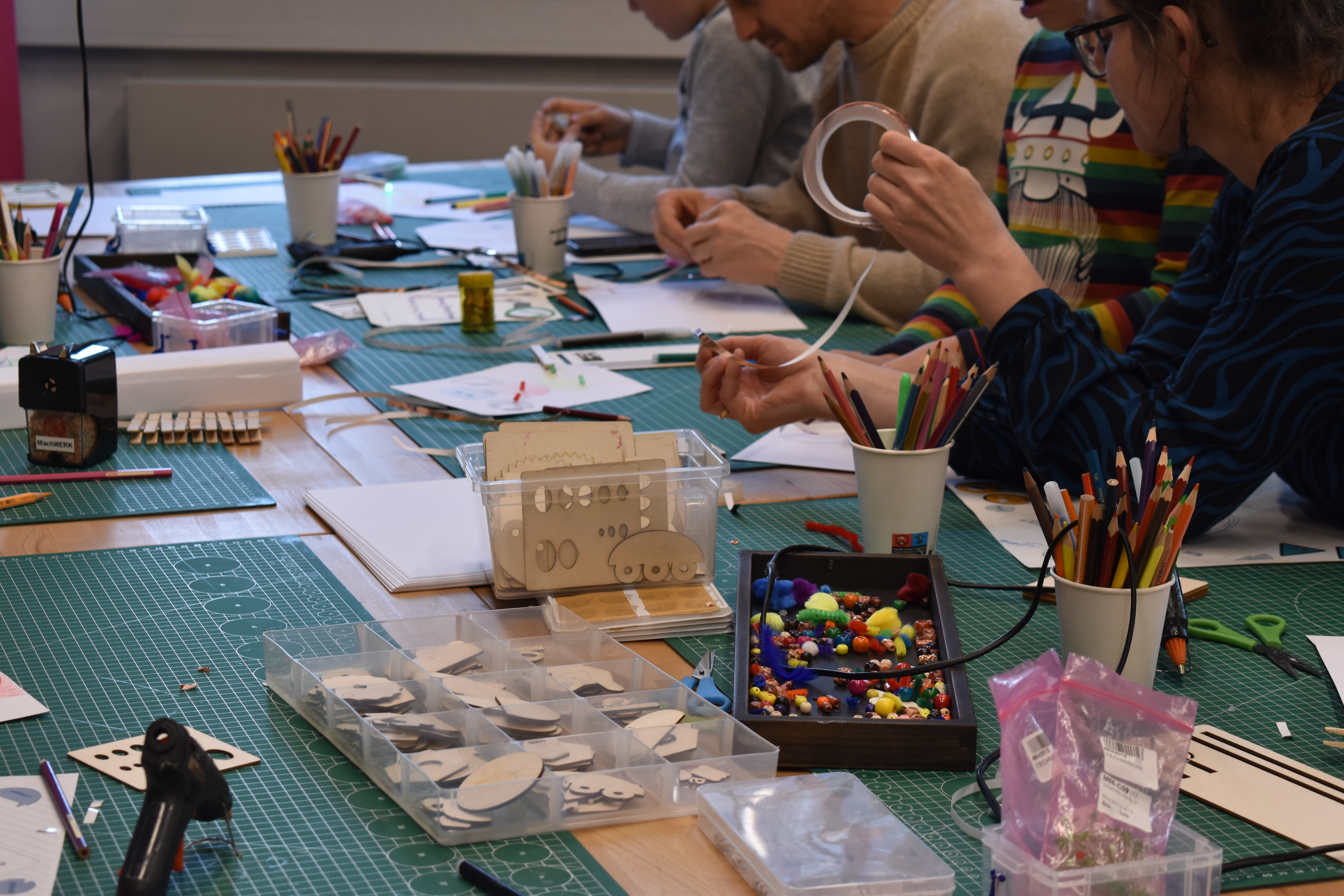 Mehrere Personen sitzen an einem Tisch mit Bastelmaterialien wie Scheren, Klebeband, Stiften und ausgeschnittenen Papierformen