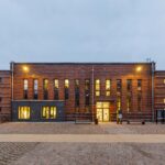 Ansicht eines Backsteingebäudes mit Flachdach in der Abenddämmerung mit erleuchteten Fenstern.