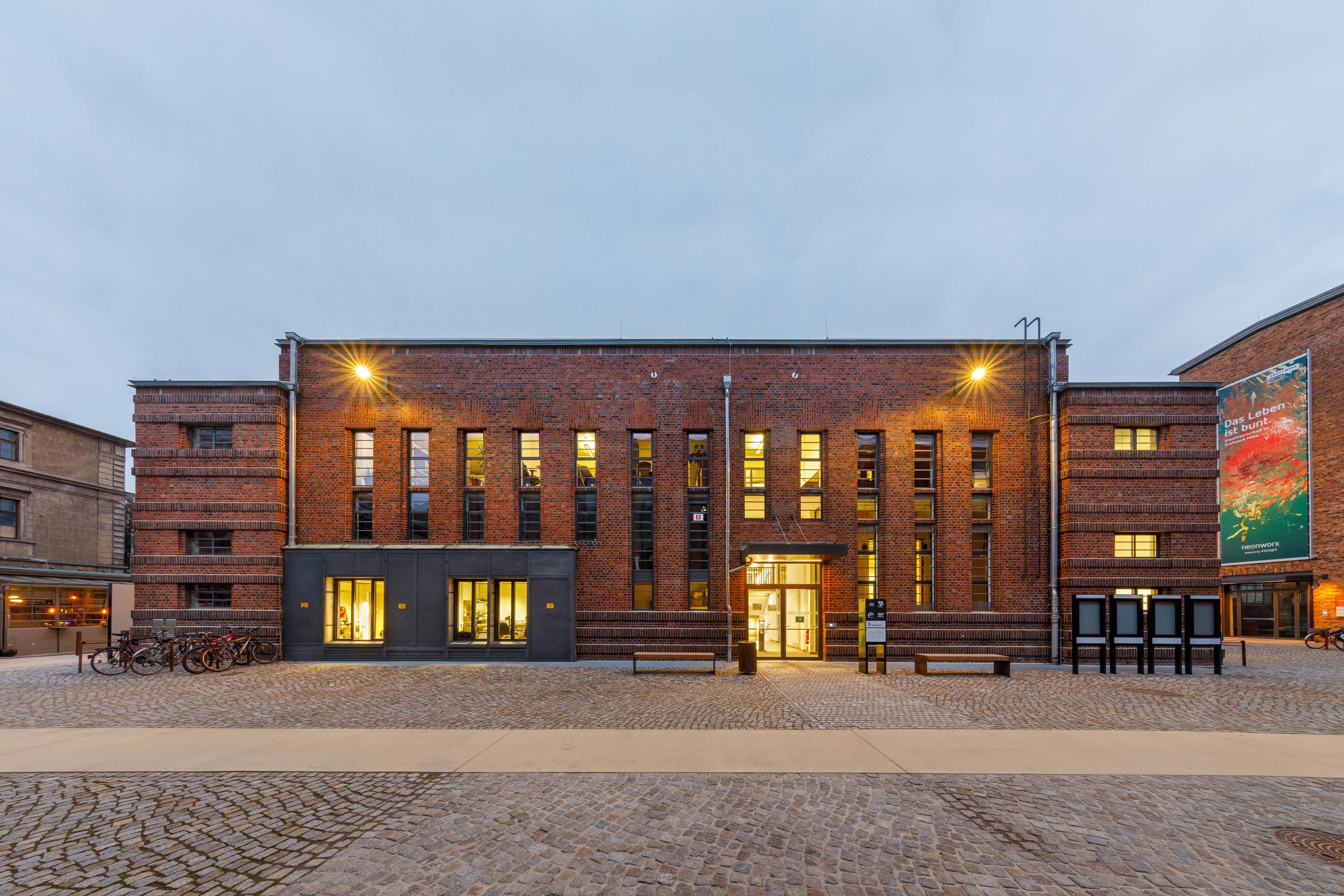 Ansicht eines Backsteingebäudes mit Flachdach in der Abenddämmerung mit erleuchteten Fenstern.