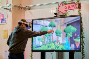 Ein Jugendlicher mit VR-Brille vor einem Display, ein Arm ist greifend nach vorne ausgestreckt