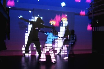 zu sehen sind zwei Personen, die sich in einer Projektion aus Lichtpixeln bewegen