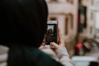 Frau mit Kopftuch hält Smartphone und fotografiert ein Gebäude in einer Straße
