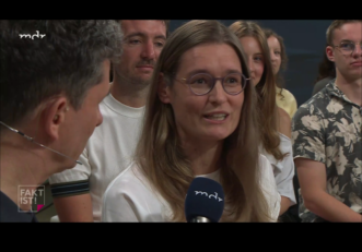 Kristina Richter spricht ins Mikron des mdr, daneben der Moderator, dahinter das Publikum