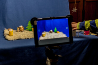 Ein Tablet unscharf im Vordergrund, dahinter ein Trickfilmsetup mit Felluntergrund, Figuren aus Kork und gelben Überraschungseiern