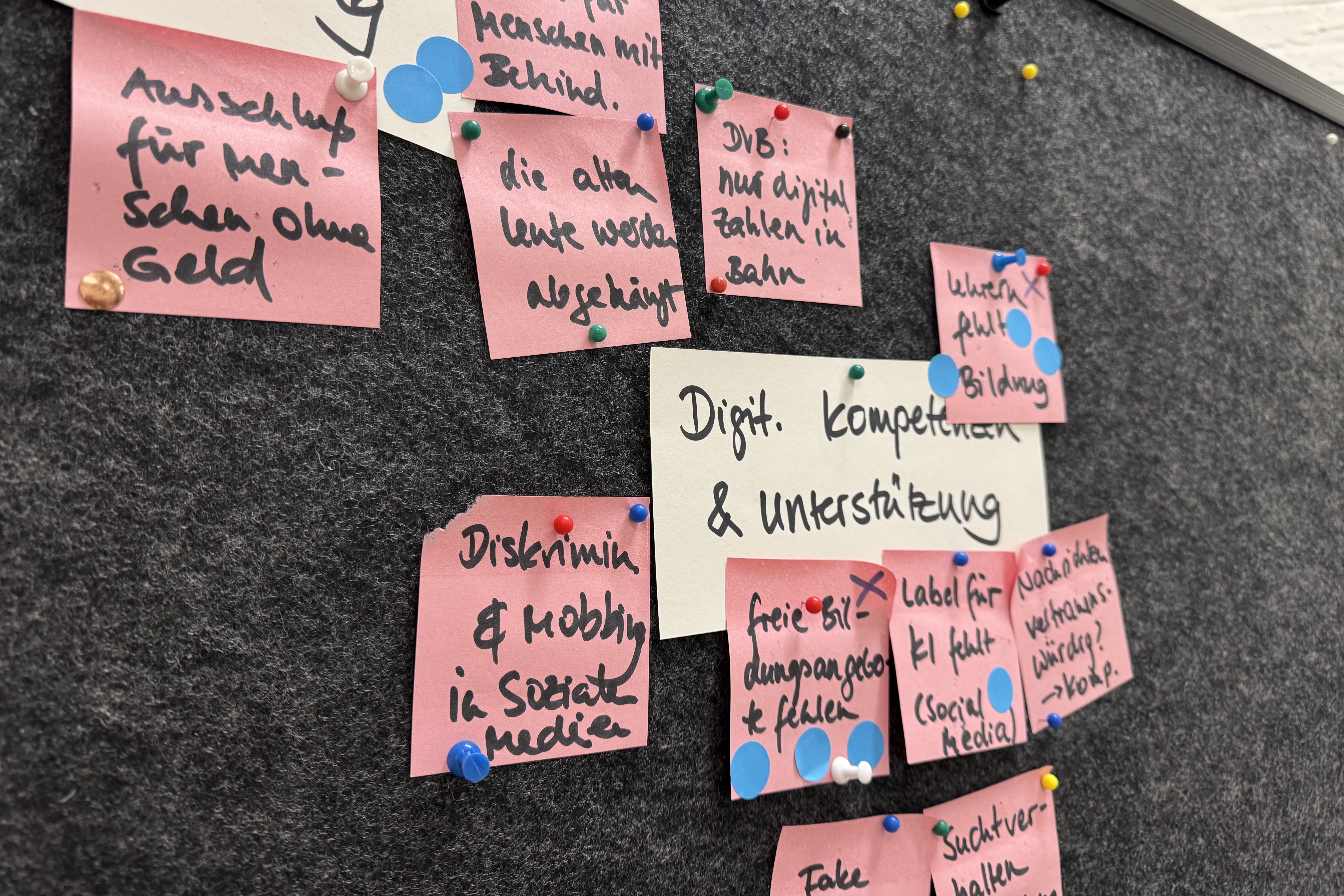 Pinnwand mit rosa und weißen Klebezetteln. Lesbar ist u.a. "Digitale Kompetenzen und Unterstützung"
